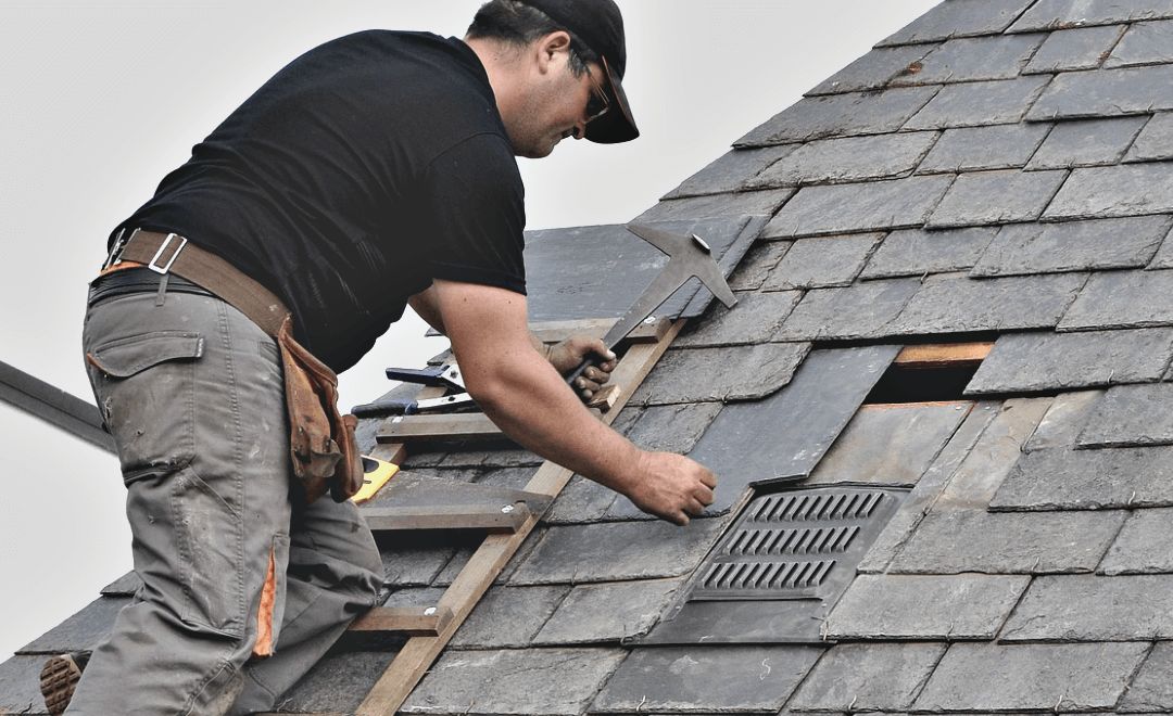 Roofer replacing a section of slate on a pitched roof